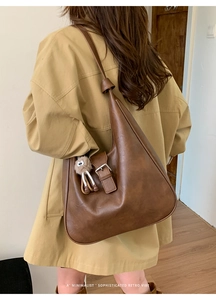 Détail d'un grand sac à bandoulière marron vintage avec breloque en peluche vue de côté