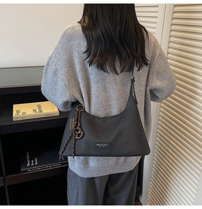 Detail view of a charcoal gray hobo bag featuring a woven rope charm and logo patch