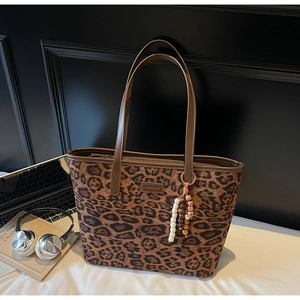 Detail of leopard print tote bag with brown leather handles and a beaded keychain charm