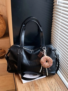 Large black faux leather tote bag with silver zippers and a cute plush charm on a table