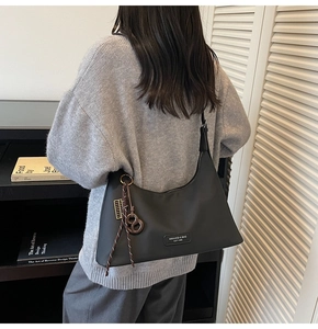 Detail of a black hobo bag with braided charm and metal zipper for autumn style