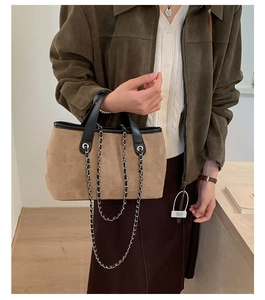 Detail of brown suede tote bag with black leather handle and woven metal chain strap