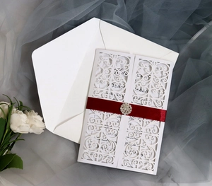 Detailed laser cut lace wedding invitation with red satin ribbon and rhinestone buckle