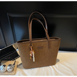 Close-up of brown suede tote bag featuring ethnic bead charm and durable zipper detail