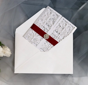 Detailed laser-cut wedding invitation with burgundy ribbon and rhinestone brooch
