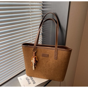 Close-up of brown suede tote bag featuring a leather logo patch and beaded tassel detail