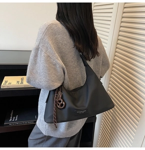 Detail view of black crescent shoulder bag with metal logo and knotted charm accessory