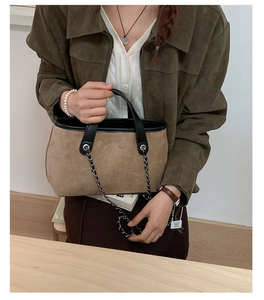 Detail of brown suede bucket bag with black leather trim and silver metal chain strap