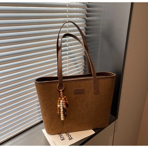 Close-up of brown frosted suede tote bag featuring wooden bead charm and embossed label