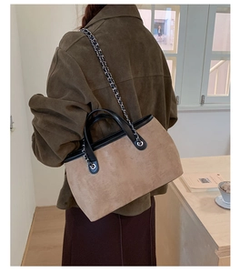 Detail of suede bucket bag with black leather trim and silver chain shoulder strap