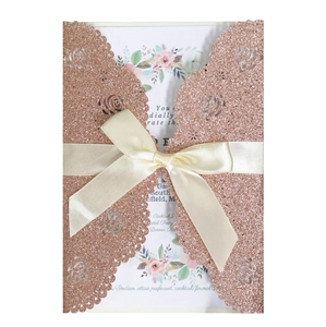 Detail of rose gold laser cut wedding invitation with glitter floral texture and cream ribbon