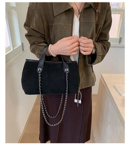 Detail of black suede tote bag with silver chain and leather trim worn by model
