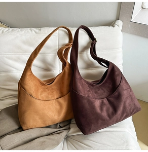 Détail de sacs hobo en daim marron et camel posés sur un canapé blanc élégant