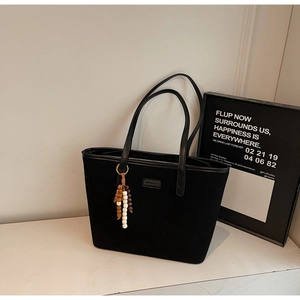 Close-up of black matte tote bag featuring beaded tassel charm and elegant logo detail