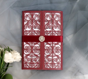 Close-up of laser-cut wedding invitation with red satin ribbon and rhinestone buckle detail