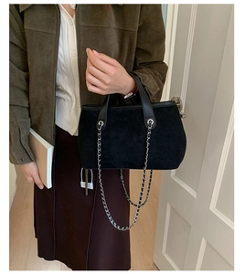 Detail of vintage black suede tote bag with leather handles and decorative metal chains