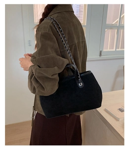 Detail view of a black suede bucket bag worn crossbody by a model in a brown jacket