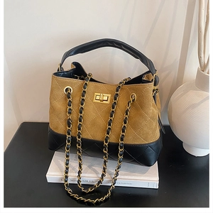 Detail of quilted suede bucket bag with gold turn-lock and chain strap on a book