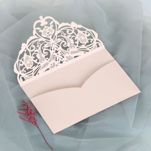 Detail of pink laser-cut floral lace invitation envelope on soft blue fabric
