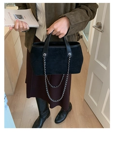 Detail of black suede tote bag featuring silver chain handles and a matte finish texture