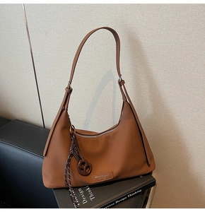 Detail of a brown textured crescent bag with brand tag and woven ball charm on a sofa