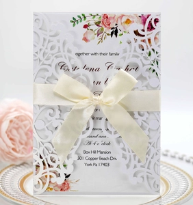 Detailed laser cut floral wedding invitation with cream satin bow on decorative plate