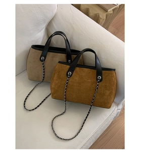 Detail of suede tote bags with chain straps and leather handles on a white sofa