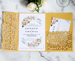 Detail of laser-cut gold wedding invitation set with floral card on marble surface