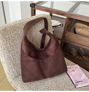 Détail d'un grand sac cabas en suédine marron posé sur une chaise tressée élégante