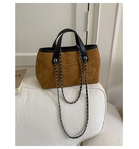 Detail of a brown suede bucket bag with black leather trim and elegant metal chain strap