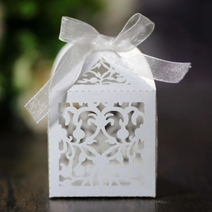 Detail view of laser-cut white wedding favor box with intricate vine pattern and ribbon bow