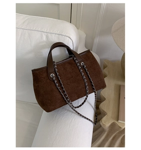 Detail of dark brown suede bucket bag with silver chain strap on a white sofa
