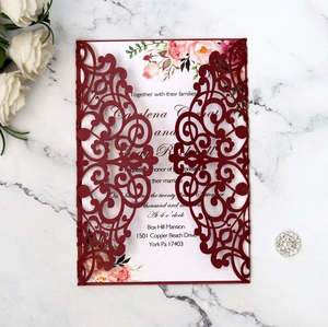 Detail of burgundy laser-cut wedding invitation with elegant floral insert on marble
