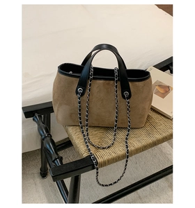 Detail of suede bucket bag with leather handles and chain strap on a vintage chair
