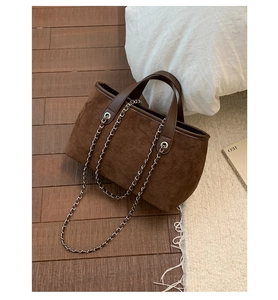 Close-up of brown suede bucket bag featuring silver metal chain and soft leather handle