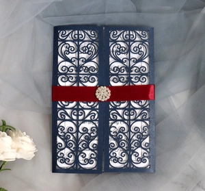 Detail of laser-cut navy blue wedding invitation with red ribbon and rhinestone brooch
