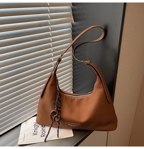 Detailed close-up of a caramel brown leather hobo bag with textured grain and brand logo