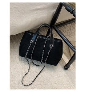 Close-up of black suede tote with leather trim and woven silver chain straps