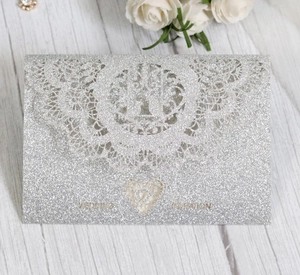 Detailed laser-cut silver glitter wedding invitation with intricate lace heart patterns