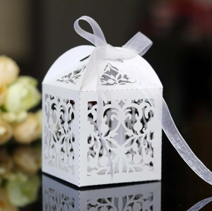 Close-up of white laser-cut wedding candy box with intricate floral patterns and ribbon bow