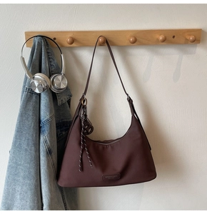 Detail view of brown nylon hobo bag featuring a metal logo plate and woven cord pendant