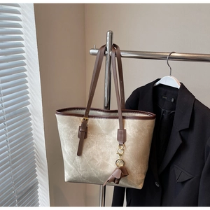 Detail of beige tote bag with brown leather trim and cute elephant charm on a metal hanger