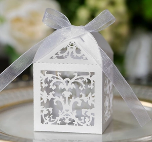 Detail of white laser-cut wedding candy box with elegant vine patterns and organza ribbon
