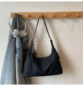 Detailed macro of a black crescent shoulder bag with brand logo and woven pendant charm