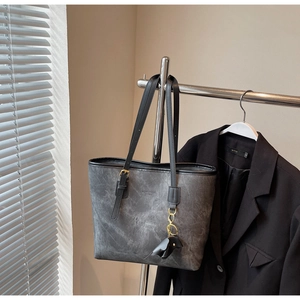 Detail of grey washed texture tote bag with black strap and cute dog charm on a rack