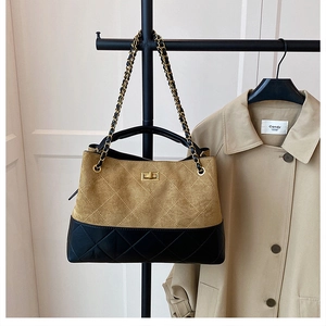 Detail of a large bucket bag with brown suede, black leather, and gold chain strap