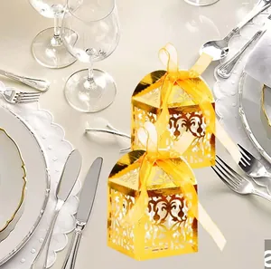 Close-up of golden laser-cut lace candy boxes with yellow organza ribbon on a dining table