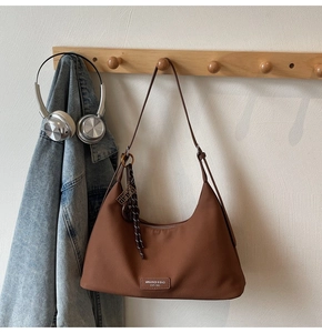 Close-up of brown textured leather shoulder bag with logo tag and woven knot charm