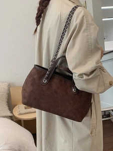 Dark brown suede bucket bag with silver chain strap worn with a beige trench coat