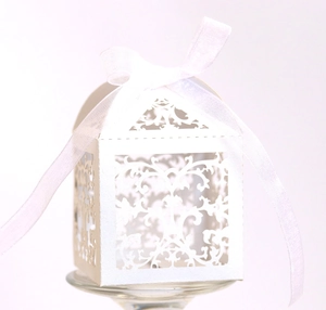 Close-up of white laser-cut floral wedding candy box with a sheer organza ribbon bow